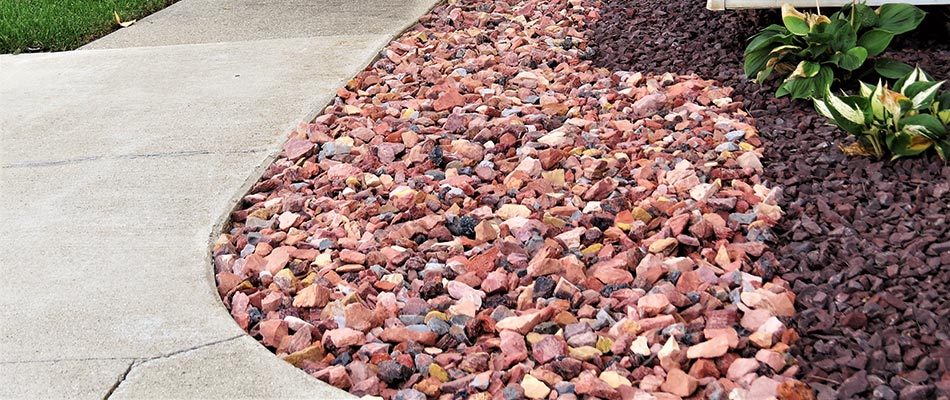 A landscape bed topped with lava rock mulch alongside a paved sidewalk on a property in Fishers, IN.